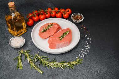 Beyaz seramik tabakta çiğ biftek, domates, tuz ve biber.