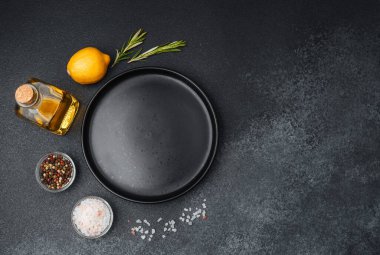 Bir limon, bitkiler ve yağ karanlık bir yüzeyde boş bir tabağın yanına dizilir..