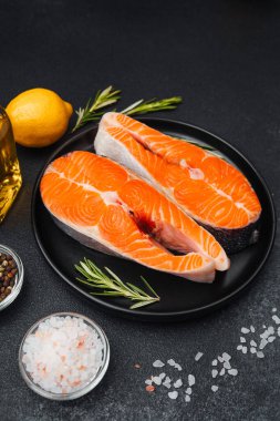 Somon filetoları siyah bir tabağa konur. Bitkiler, limon ve yağın yanına..