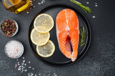 Canlı bir somon filetosu, bir tabakta limon dilimleri ve baharatlarla sıralanır..