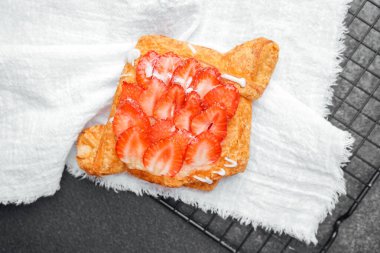 Dilimlenmiş çilekle kaplı yumuşak bir hamur işi soğutma rafında duruyor, eğlenmeye hazır..