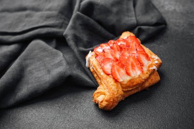 Çilekli hamur işi koyu bir yüzeyde, desenli kumaşın yanında durur..