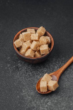 Esmer şeker küpleri düzgün bir şekilde bir kâseye yerleştirilmiş ve kaşık desenli bir yüzeye yerleştirilmiş..