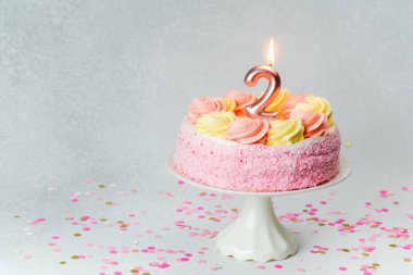 Etrafı konfetilerle çevrili iki mumlu enfes pembe bir pasta..