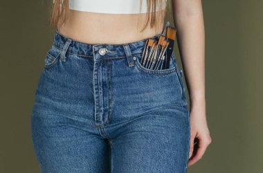 DIY projesi ya da ev yenileme konsepti için cebinde boya fırçası olan kot pantolonlu kadın beli