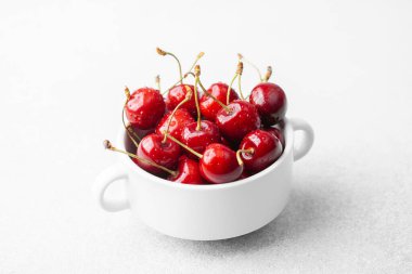 Minimum meyve çerezi veya sağlıklı yiyecek konsepti için beyaz arka planda beyaz kasedeki kirazlar