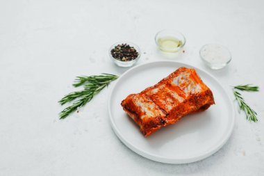 Beyaz tabakta marine edilmiş domuz pirzolası, biberiye ve baharatlı.