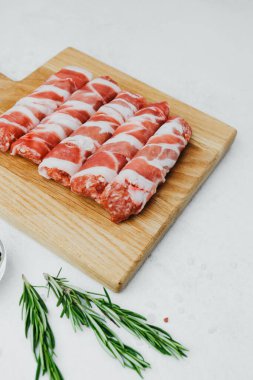 Domuz pastırmasına sarılı sosisli börekler, ahşap tahtada otlarla.