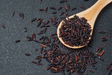 Siyah pirinçle dolu tahta kaşık ve koyu arkaplana dökülen tahıllar.