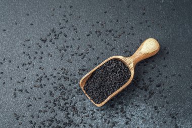 Koyu arkaplanda siyah susam tohumlarıyla dolu ahşap kepçe