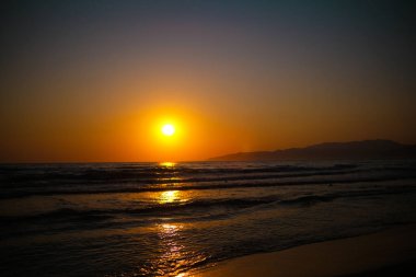 Parlak turuncu gün batımı suyun üzerinde parlayan ışıkla