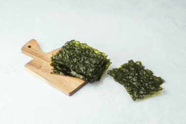 Ahşap kesme tahtasında gri arka planda kavrulmuş yosun atıştırmalığı.