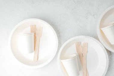 Beyaz tek kullanımlık tabaklara dağılmış beyaz kağıt bardaklar ve ahşap çatallar.