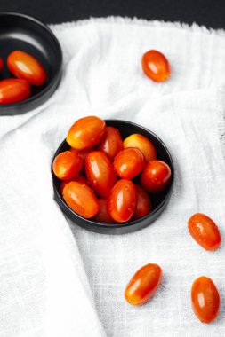 Siyah bir kasede su damlacıklarıyla parlayan taze kiraz domatesleri..