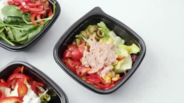 Renkli sebze ve ton balığı gibi taze malzemelerle dolu birden fazla canlı ve sağlıklı salata hazır yemek için siyah kaplarda sunuluyor..