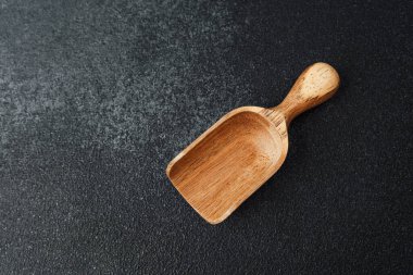 Ahşap kepçe, zarif tasarımını sergileyen koyu dokulu bir arka plana dayanır..