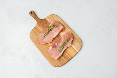 Biberiyeyle süslenmiş iki çiğ domuz pirzolası ahşap bir kesme tahtasına oturur..