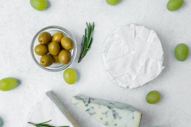 Zeytin ve üzümlerle çevrili kremalı ve mavi çeşitlerden oluşan peynir çeşitleri..