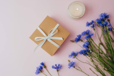 Arkaplanda mum ve çiçek olan bir hediye kutusu.