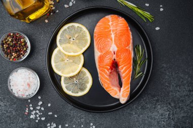 Canlı bir somon filetosu, bir tabakta limon dilimleri ve baharatlarla sıralanır..