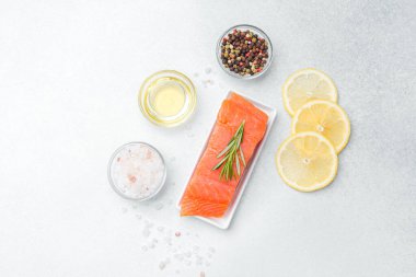 Taze somon filetosu hafif bir yüzeyde bitkiler, baharatlar ve limon dilimleriyle düzenlenir..