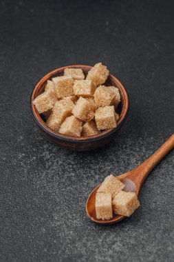 Esmer şeker küpleri düzgün bir şekilde bir kâseye yerleştirilmiş ve kaşık desenli bir yüzeye yerleştirilmiş..