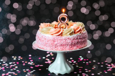 Doğum günü pastası pembe krema ve tek bir mumla süslenmiş, etrafı şenlikli konfetilerle çevrili..