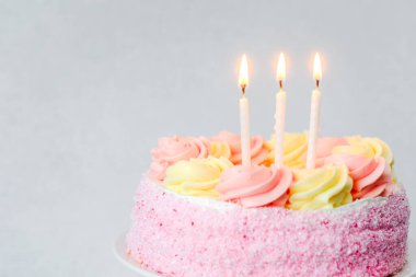 Pastel bir doğum günü pastasının üzerinde pembe ve sarı şekerli üç mum duruyor..