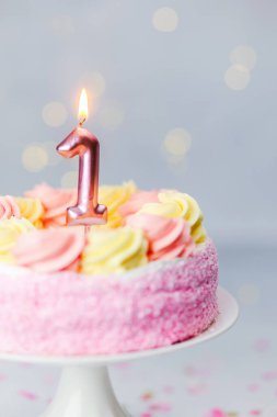 Pembe ve sarı kremayla süslenmiş kutlama pastası, bir numaralı mumu içeriyor..