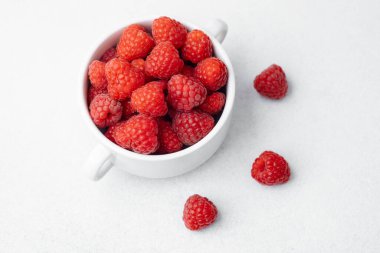 Ahududu, organik gıda veya vejetaryen diyet konsepti için hafif yüzeyde serpiştirilmiş böğürtlenlerle beyaz kasede.