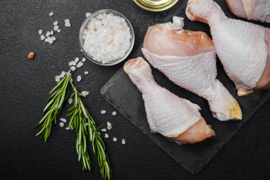 Siyah tahta üzerine yerleştirilmiş tavuk budu, otlar ve tuzlu.