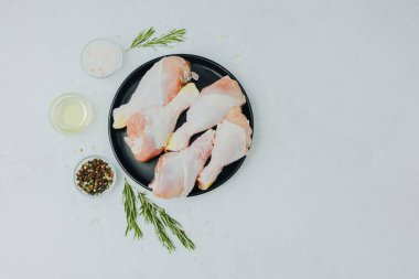 Biberiye ve baharatlı siyah tabakta çiğ tavuk budu.