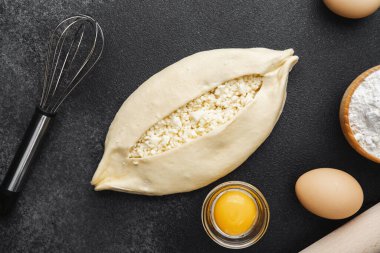 Süzme peynirli çiğ khachapuri ve siyah arka plandaki malzemeler.