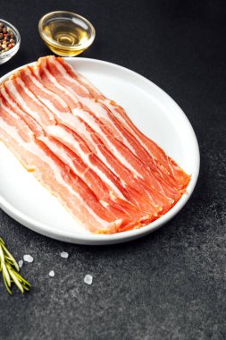 Beyaz tabakta çiğ domuz pastırması, biber, tuz ve biberiye.