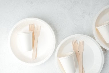 Beyaz tek kullanımlık tabaklara dağılmış beyaz kağıt bardaklar ve ahşap çatallar.