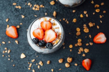 Yoğurtlu granola parfe, koyu arkaplanda çilek ve yabanmersini.