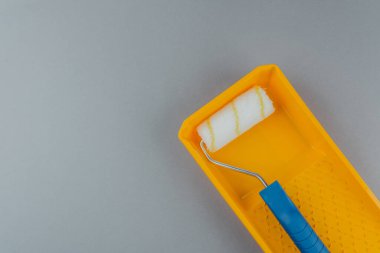 Ev geliştirme ve yenileme konsepti için gri arka planda sarı tepsinin içinde mavi saplı boya silindiri