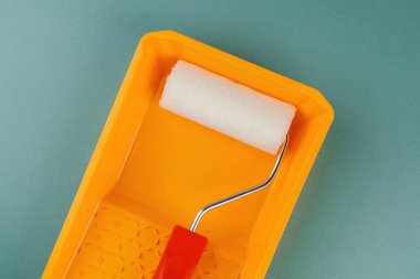 Yeşil arka planda sarı tepside kırmızı saplı boya silindiri DIY yenileme ve ev geliştirme konsepti için