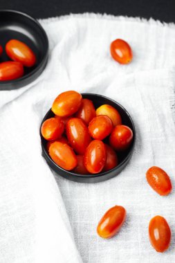 Siyah bir kasede su damlacıklarıyla parlayan taze kiraz domatesleri..