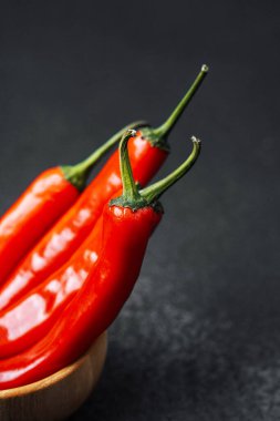 Koyu bir yüzey üzerinde ahşap bir kasede dizilmiş üç canlı kırmızı biber..