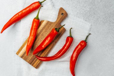 Ahşap kesme tahtasına yerleştirilmiş parlak kırmızı biberler hazırlanmaya hazır..