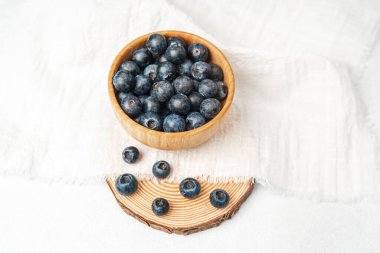 Olgun yaban mersiniyle dolu bir kase, kumaşın üzerindeki ahşap bir dilimin üzerinde duruyor..