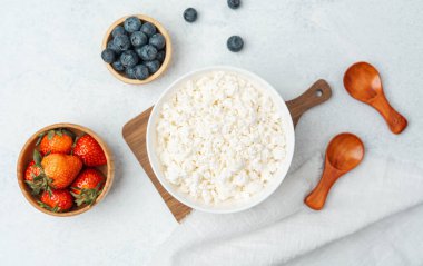 Bir kase süzme peynir hafif bir yüzeyde çilek ve yabanmersinleriyle çevrilidir..