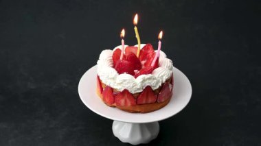 Krem şanti ve taze çilekle süslenmiş küçük bir çilekli pasta. Parlayan üç doğum günü mumuyla aydınlatılmış..
