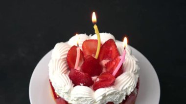Lezzetli bir doğum günü pastası, taze kırmızı çilekler ve beyaz kremayla süslenmiş, parlak yanan mumlar içeriyor, mutlu bir kutlama için mükemmel..