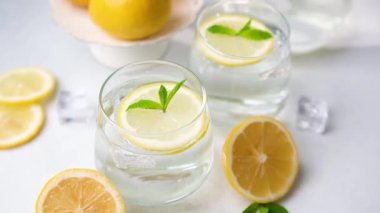 İki bardak ferahlatıcı limon suyu taze nane yaprakları ve buz küpleri hafif bir arka planda güzelce düzenlenir, yaz içeceği için mükemmeldir..