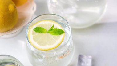 Limon dilimli ferahlatıcı bir bardak su ve taze nane yaprakları, beyaz bir masada buz küpleriyle serinliyor..