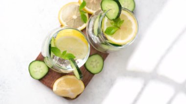 Taze limon, salatalık ve temiz bardaklardaki nane suyu ahşap bir tahtanın üzerinde duruyor. Bu sağlıklı, doğal içecek ferahlatıcı sağlık faydaları sunar..