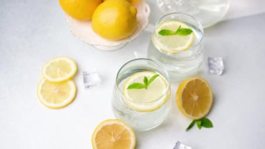 Parlak sarı limonlar, taze dilimler ve bütün meyveler soğuk suyla bardaklarda, buz küplerinde ve yeşil nane yapraklarında sergileniyor..