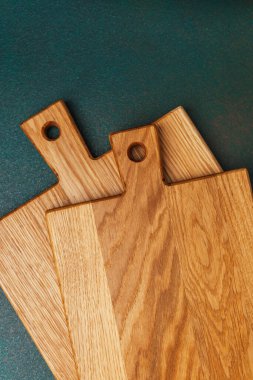 Koyu yeşil bir zemine dizilmiş üç tahta kesme tahtası seti..